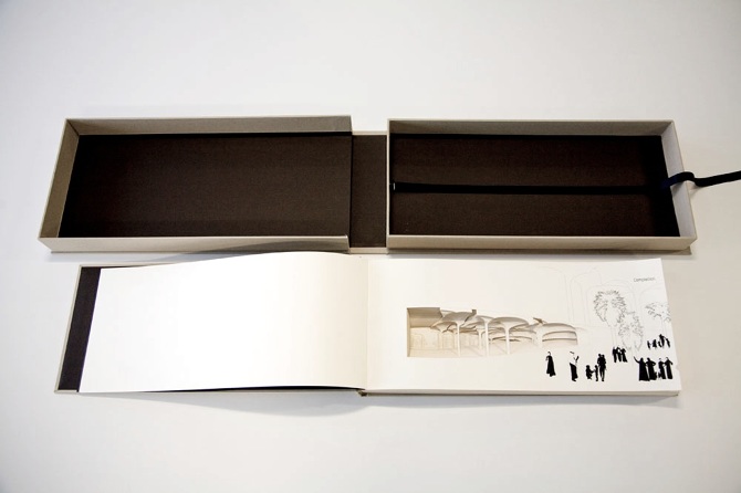 Image showing the book, open in the first page, showing the shape cut in and printed images of people walking nearby. The book's storage box is also shown, it is covered in a cream coloured fabric and has a black interior.